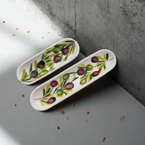 white ceramic olive holder in the shape of a small boat, decorated with olives on a white background
