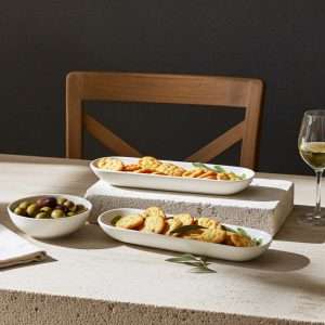 white ceramic olive holder in the shape of a small boat, decorated with olives on a white background
