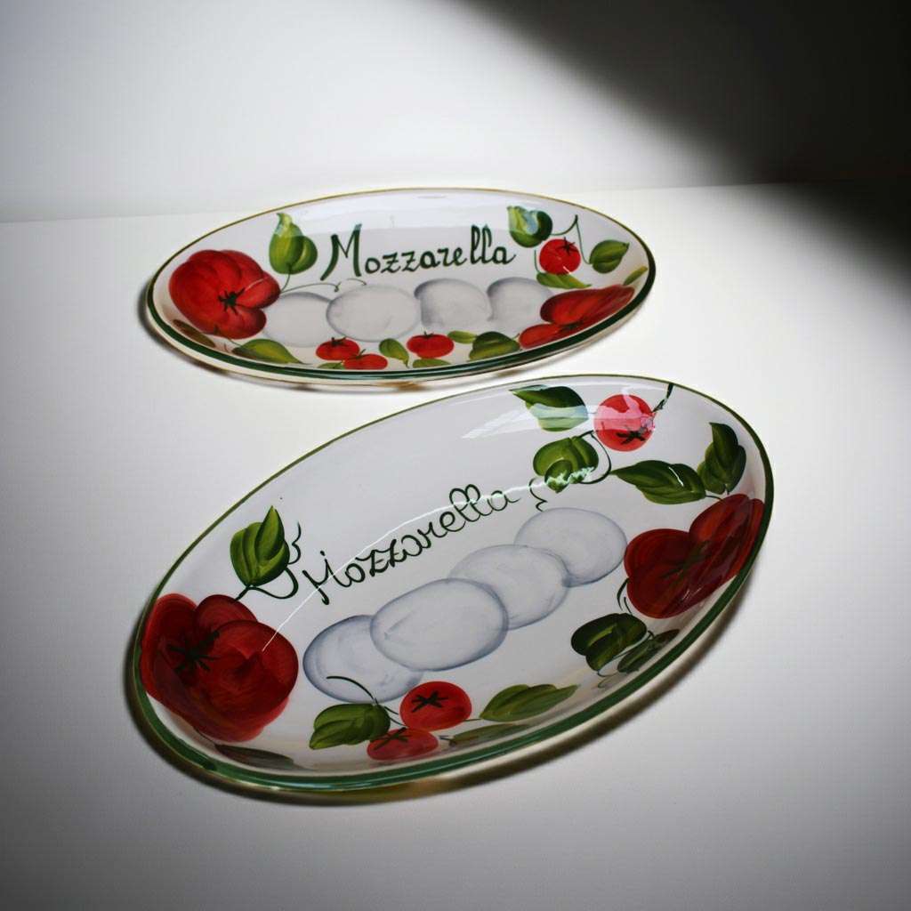 dettagli di pirofile in ceramica decorate con pomodoro e mozzarella su sfondo bianco