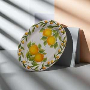 Dettaglio di vassoio moderno ovale in ceramica decorato a mano con limoni e foglie verdi su sfondo bianco