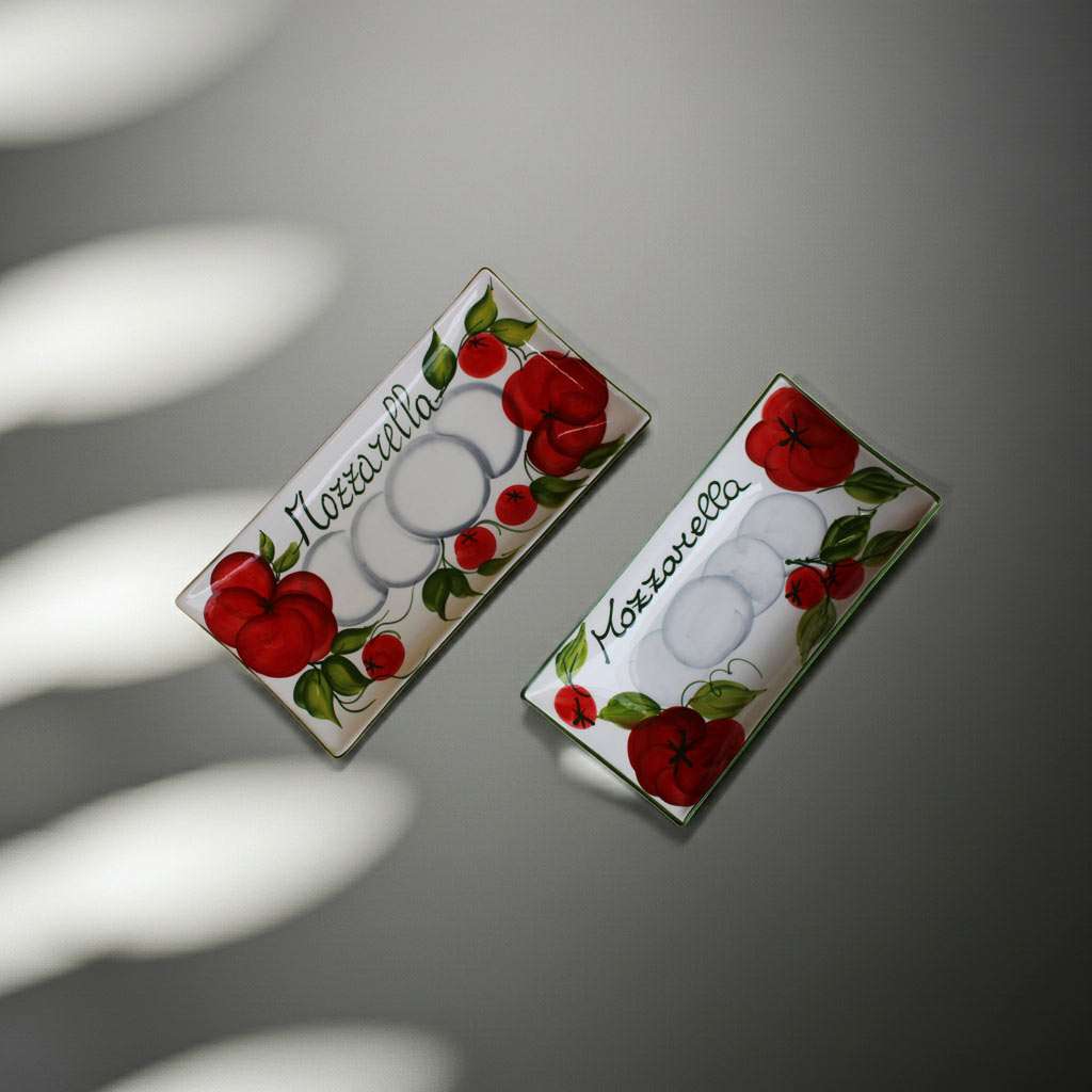 details of rectangular white ceramic trays decorated with tomato and mozzarella design on a white background