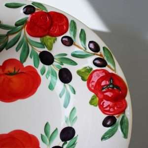 details of the hand-painted ceramic bowl with tomato and olive design on a white background.