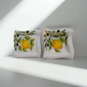square white ceramic plate decorated with lemons, leaves, and olives on a white background