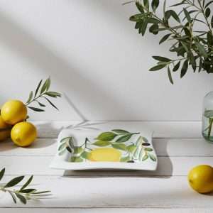 square white ceramic plate decorated with lemons, leaves, and olives on a white background