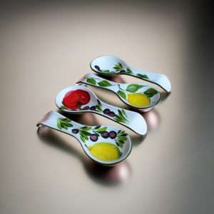 four ceramic spoon rests decorated with lemon, tomato, and olive designs on a white background