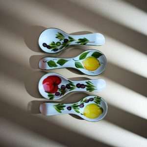 four ceramic spoon rests decorated with lemon, tomato, and olive designs on a white background